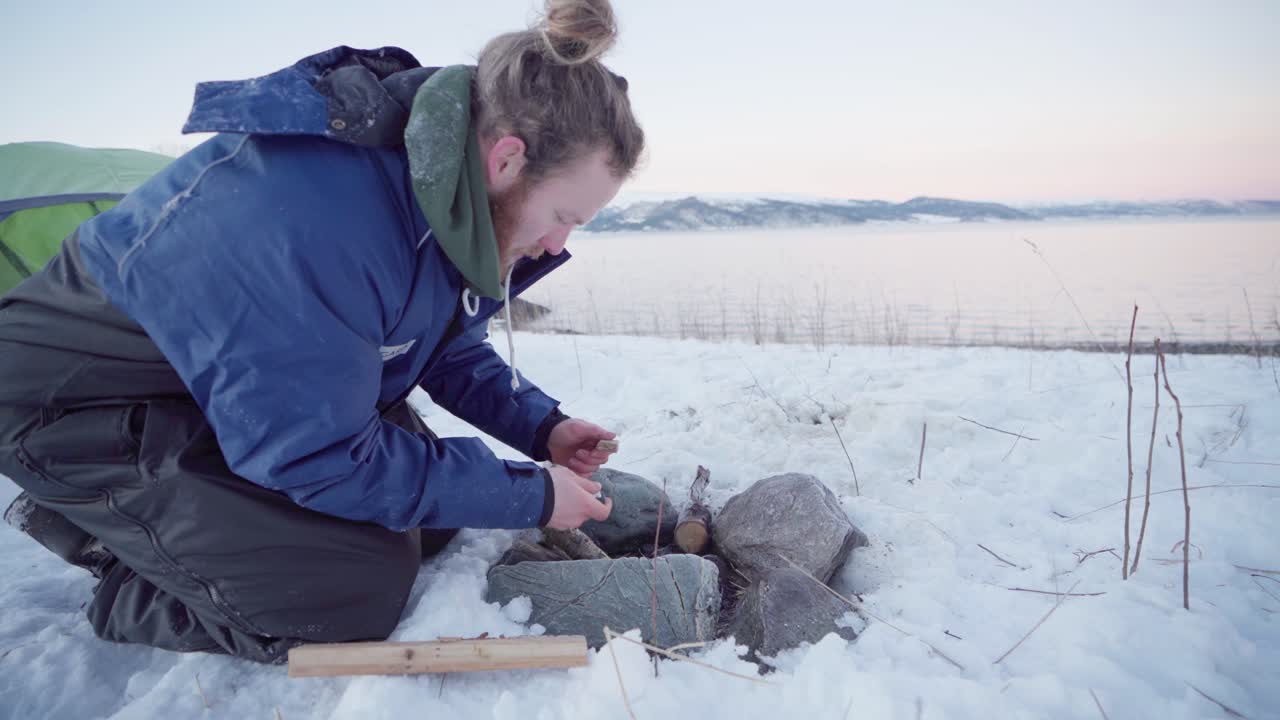 joven que tiene dificultades para hacer una fogata para una noche fría en invierno