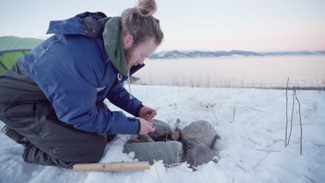 young man having a hard time making a campfire for a cold night at winter