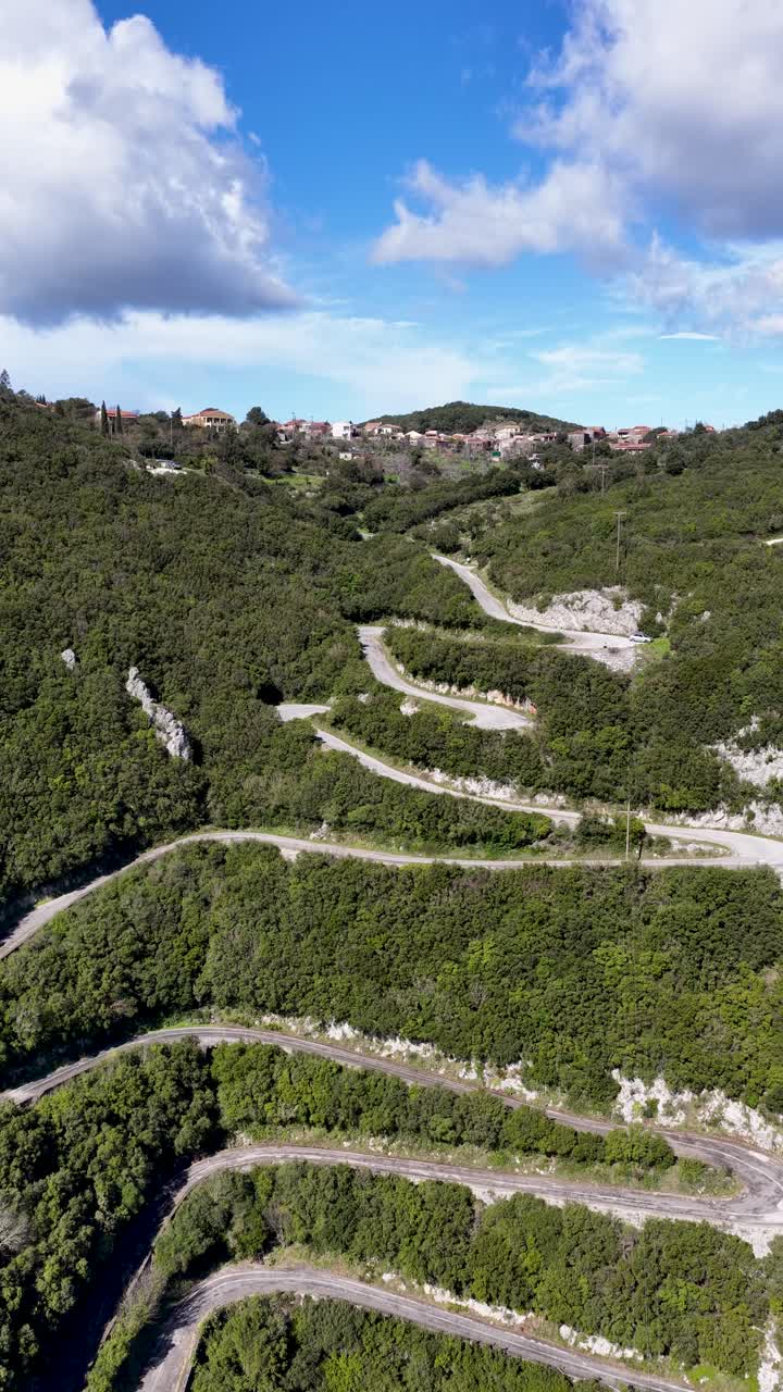 Ripresa aerea verticale di una strada di montagna estremamente tortuosa con numerosi tornanti a gomito che sale attraverso una fitta foresta verde fino al villaggio di Sokraki a Corfù