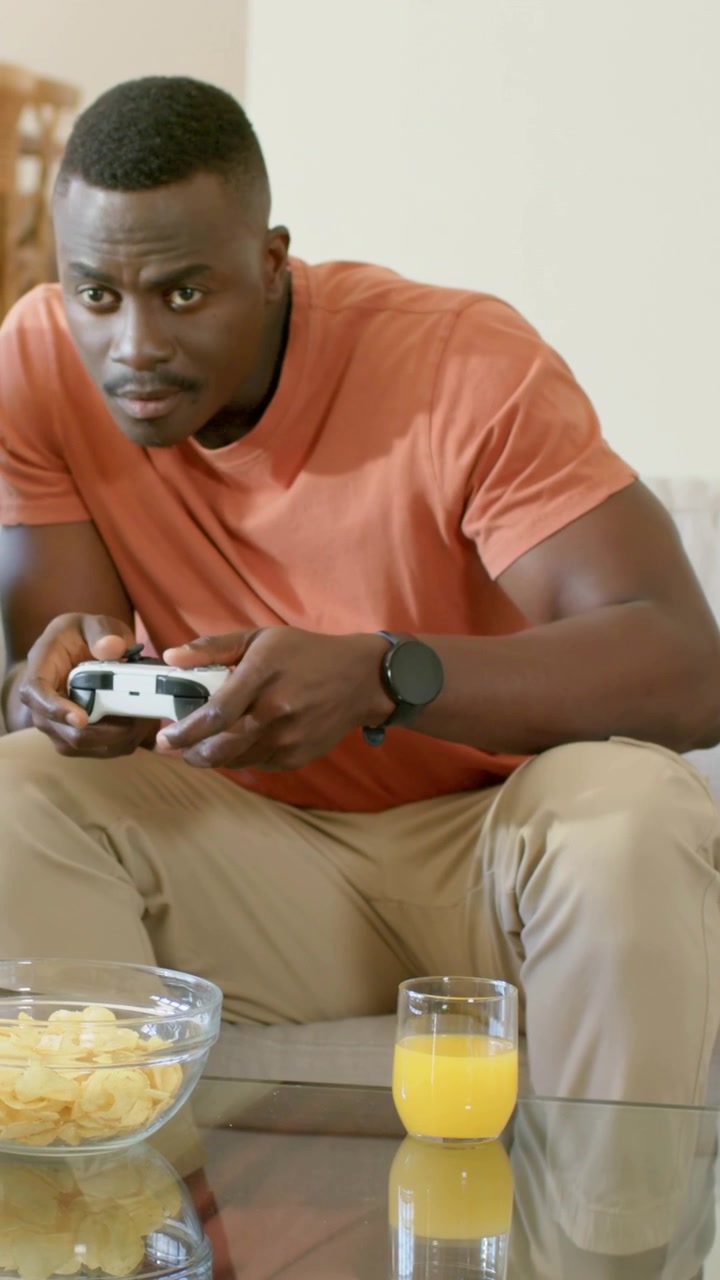 Vertical video: Leaning as game starting, man home in orange tee gripping white pad, playing to win