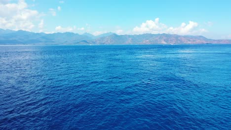 blue wavy sea around mountain island brighten by morning sunlight in lombok, indonesia, aerial panorama with copy space