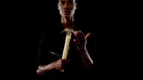 androgynous man posing with hammer against black background