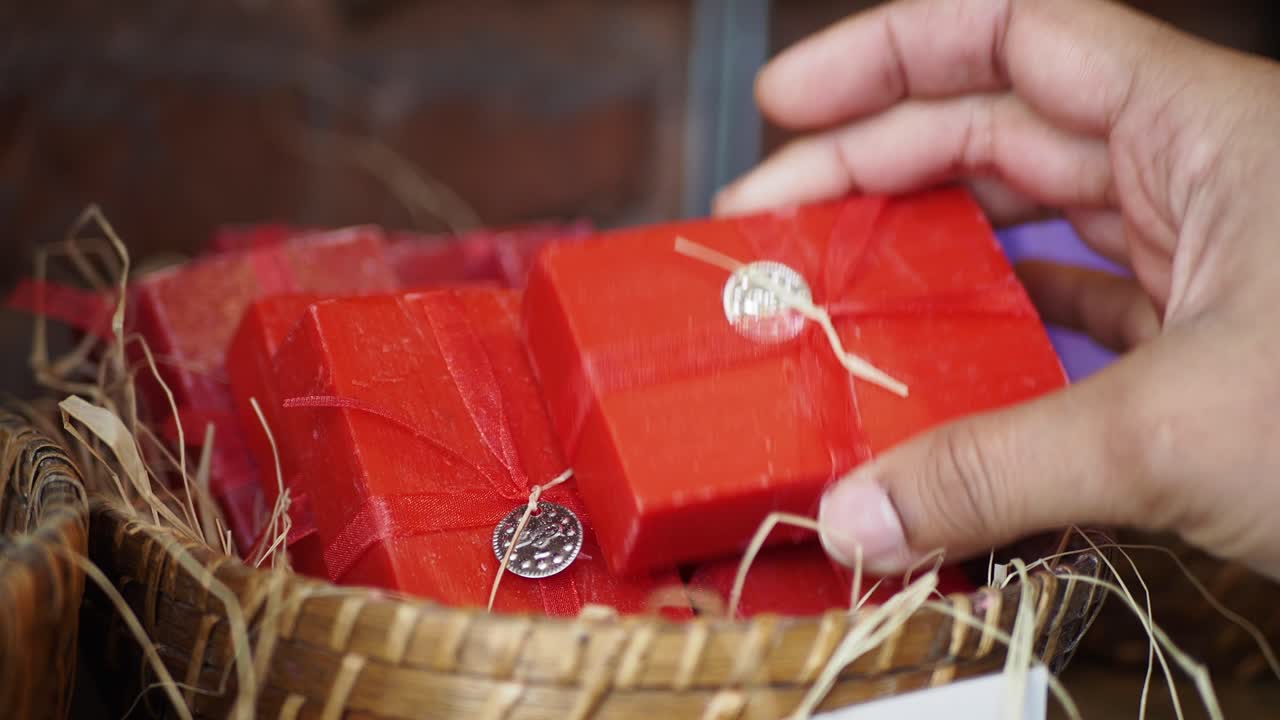 바구니에서 손으로 만든 비누의 빨간 바를 집어 들고 있는 손의 가까운 모습