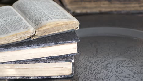 close-up tilt of old used books on decorated metal tray on table