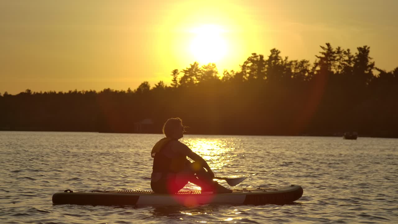linda chica sentada en paddle board fuerte puesta de sol con destello de lente slomo epic