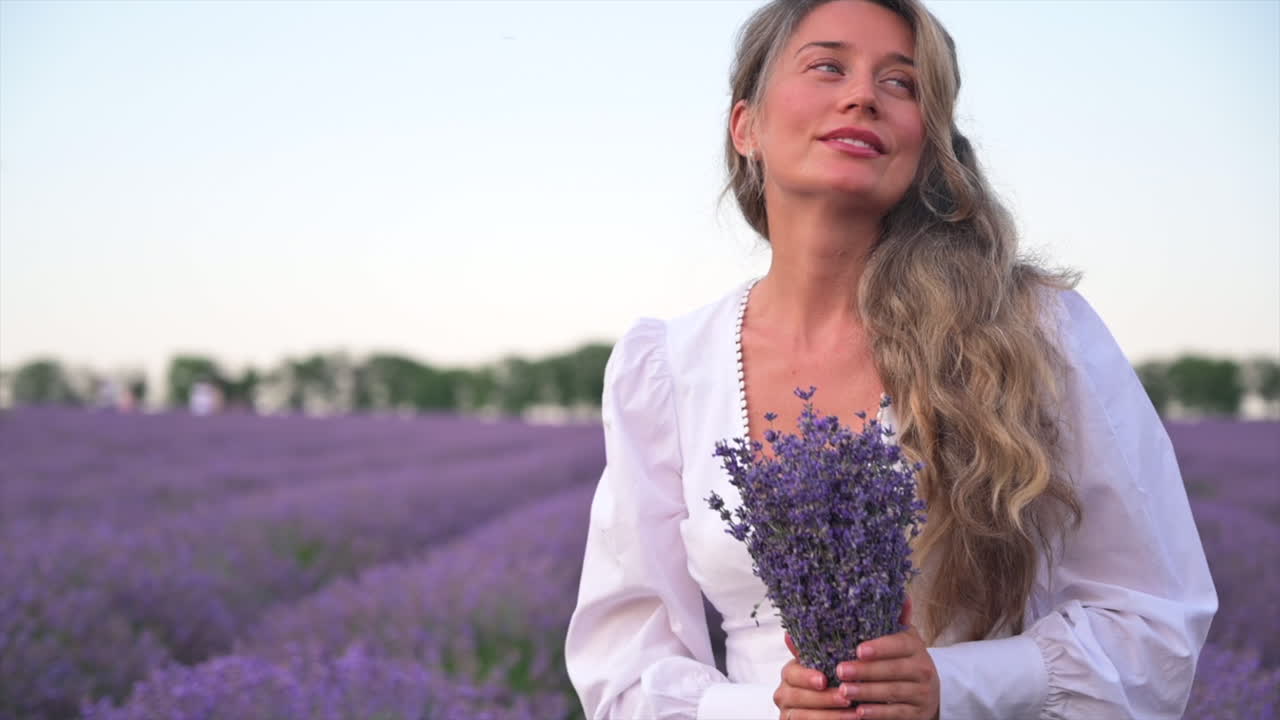 Woman in a white dress smelling a bouquet of lavender in a field