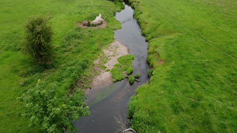 An-aerial-view-of-the-small-river-Arrow-running-through-the-green-fields-of-Warwickshire,-England