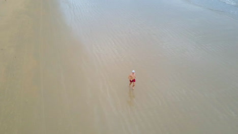 Drone-view-of-a-guy-running-on-the-beach-with-blue-water