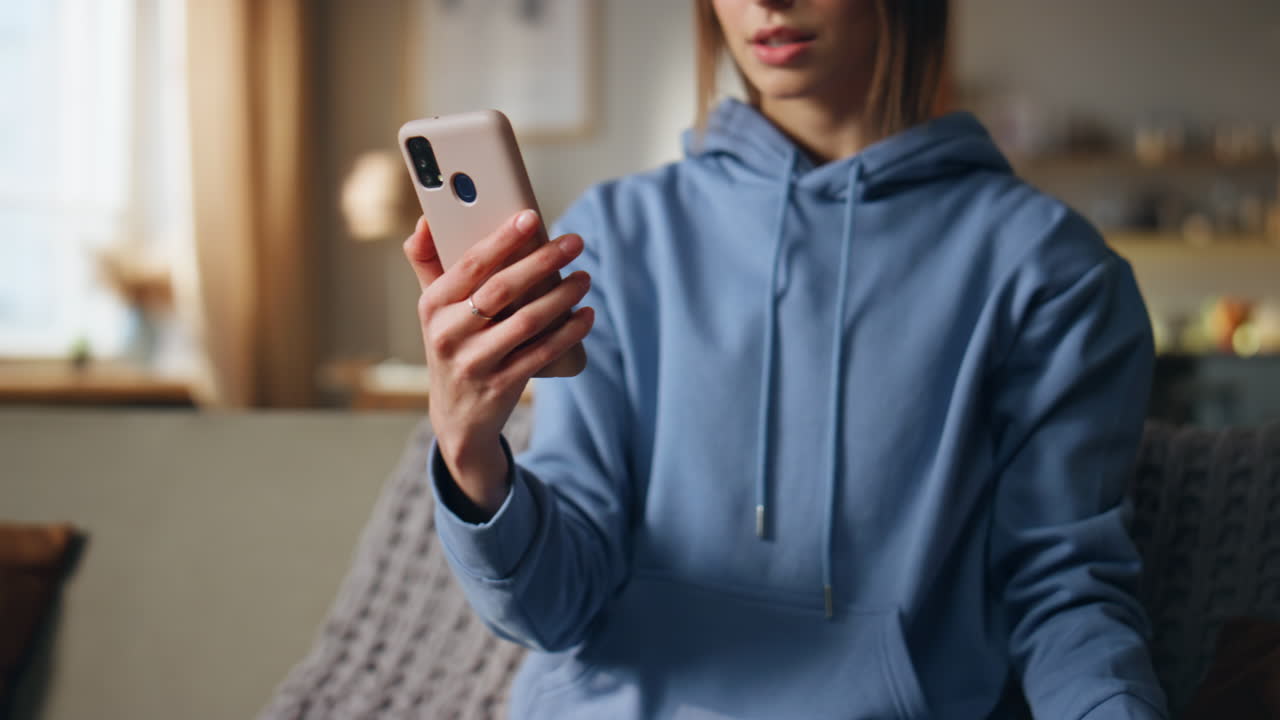 Woman in blue hoodie using smartphone indoors