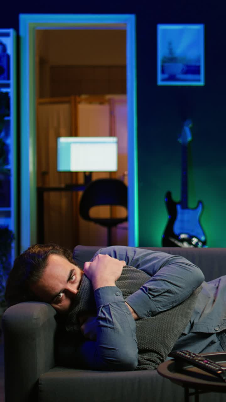 Vertical video Man laying down hugging pillow watching TV, heartbroken by upsetting movie plot