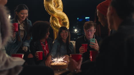 Feliz-Grupo-De-Amigos-Celebrando-Una-Fiesta-De-Cumpleaños-En-La-Azotea-Por-La-Noche-Hermosa-Joven-Disfrutando-De-Bengalas-Posando-Para-Una-Foto-Divirtiéndose-Compartiendo-Celebración