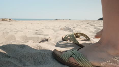 female putting on sandals on sandy beach