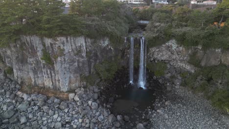 drone aerial view in south korea flying in front of a waterfall over the sea rocky area jeju island