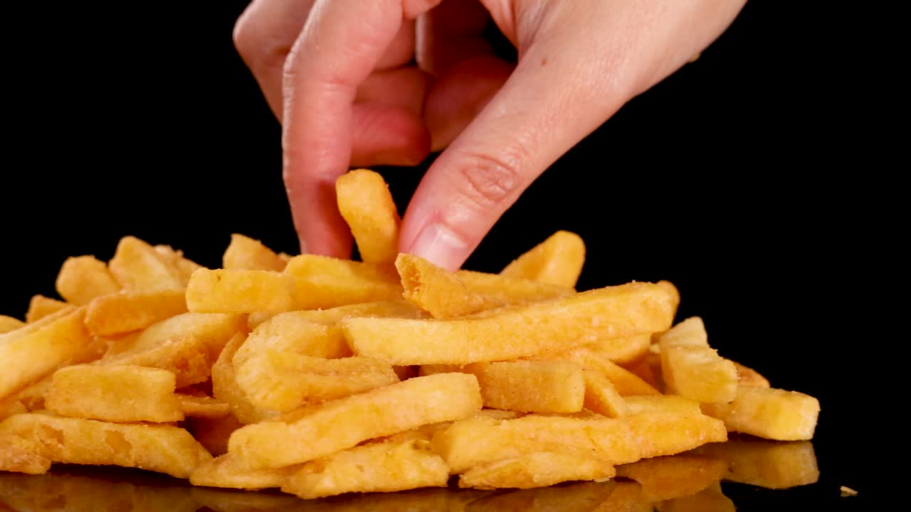 Hand rotates pile, picks up crispy French fries, studio lighting, black reflective surface, close-up