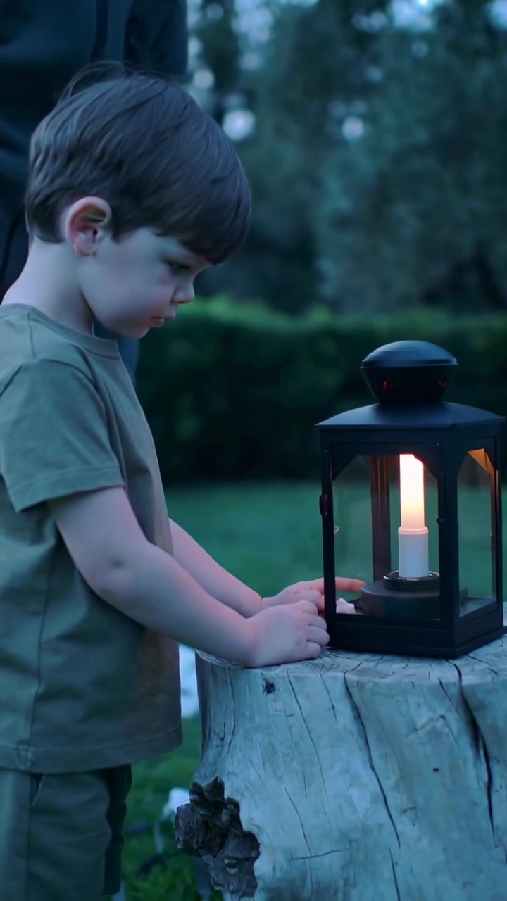 Video verticale: Posizionando una lanterna, un uomo adulto insegna a un bambino sulla luce su un ceppo al tramonto, con spazio per il testo.
