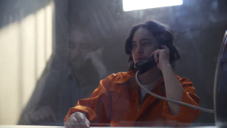 inmate speaking on phone with detective through glass partition in prison