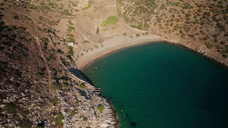 Aerial-panoramic-overview-of-lush-green-blue-water-waves-entering-calm-peaceful-bay-in-syros-greece,-varvarousa