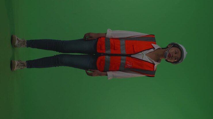 Full Body Of Asian Female Engineer With Safety Helmet Looking Around While Standing In The Green Screen Background Studio, During Sunset Or Sunrise Time