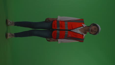 full body of asian female engineer with safety helmet looking around while standing in the green screen background studio, during sunset or sunrise time