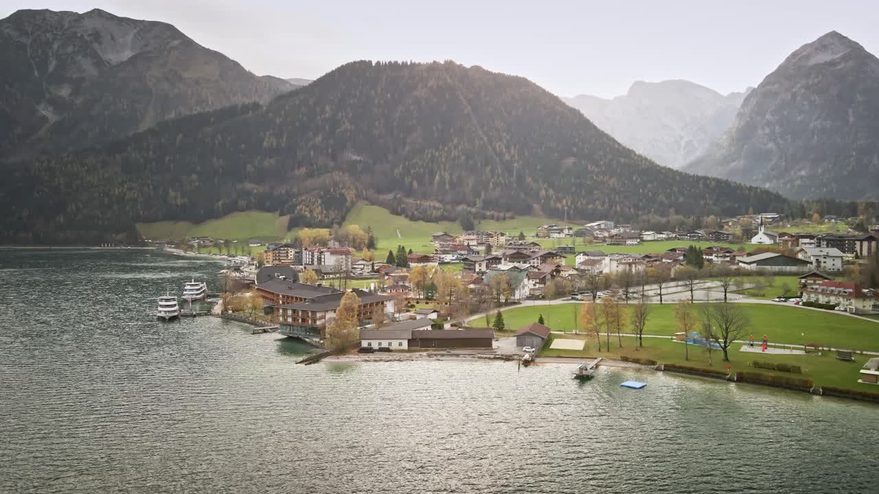 A mesmerizing drone shot from Achensee Pertisau, flying from right to left. The turquoise waters, alpine lake town, and majestic mountain backdrop create a scenic and tranquil view.