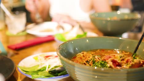 chopsticks lift noodles and beef from a steaming bowl of pho in a vibrant restaurant setting