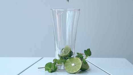 Limettenscheibe-Fällt-In-Ein-Hohes,-Glänzendes-Glas-Auf-Einem-Weißen-Tisch