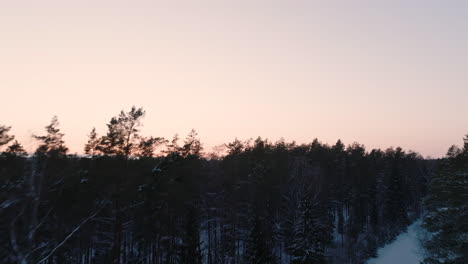 Forwards-climbing-drone-camera-view-of-winter-road-above-forest-in-the-evening-time