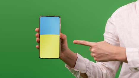 ayuda a ucrania a través del concepto de teléfono. una mujer sostiene un teléfono con la bandera de ucrania y señala con el dedo. fondo verde.