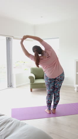 plus size biracial woman in yoga stretch at home, vertical video, slow motion