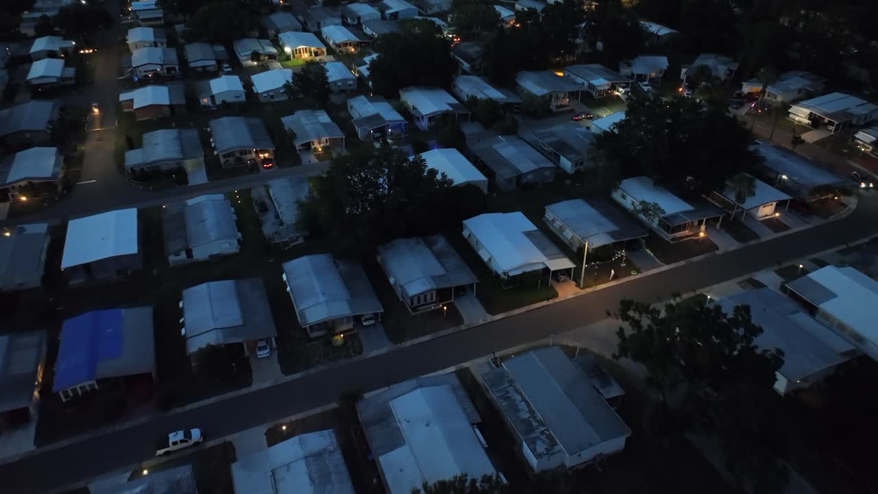Aerial view of an American neighborhood at night, with neatly arranged homes with illuminated windows, showing peaceful ambiance of suburban living under a starry sky. Top down flyover shot.