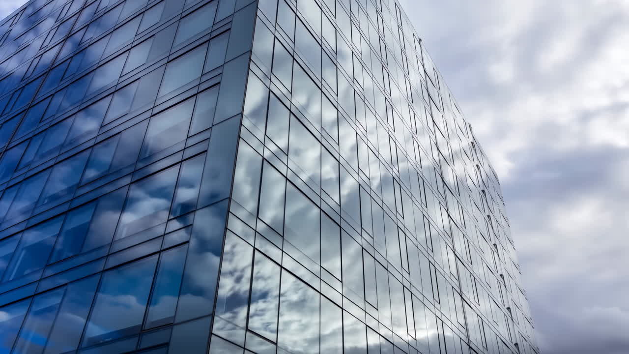 Edificio moderno de cristal que refleja nubes en movimiento en un cielo urbano