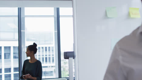 Two-diverse-happy-male-and-female-work-colleagues-talking-as-they-walk-through-office