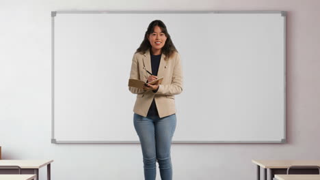 female teacher in school classroom standing in front of board taking class register