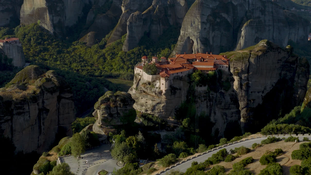 Cinematic aerial view of Meteora monastery in Greece perched on towering cliffs, dramatic rock formations and lush green valley create a breathtaking historic scene