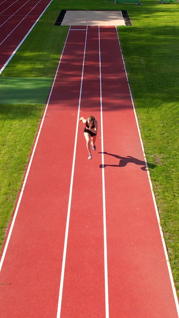 Ripresa verticale dall'alto di un'atleta che inizia il suo sprint su una pista di atletica rossa. Perfetto per contenuti su fitness, motivazione sportiva e stile di vita sano