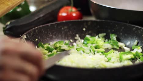 raspar cebollas blancas picadas con un cuchillo de una tabla de cortar de madera en una sartén negra con pimientos verdes picados