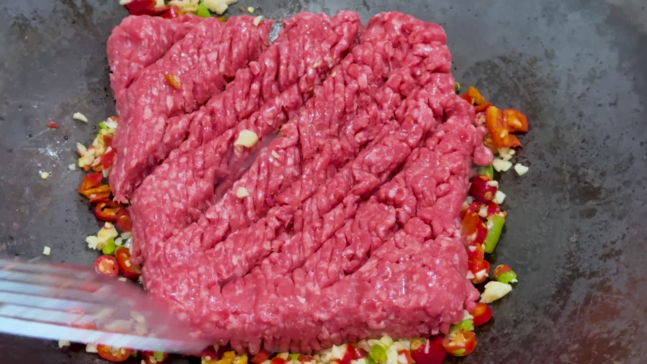 Minced beef is broken up and stir-fried with chopped spicy vegetables in a hot wok, under bright lighting, with visible steam and motion