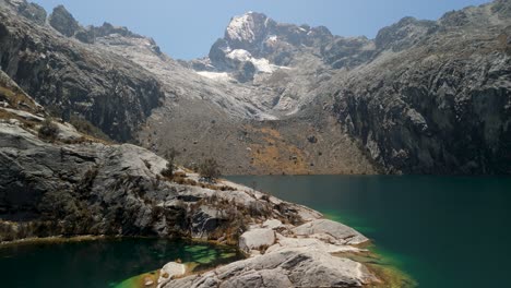 aerial flyover with a slow tilt up across vivid laguna churup, gradually revealing dramatic rocky slopes and towering andean peaks in cordillera blanca, peru
