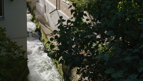 camera moves over a brick wall revealing a small river flowing between two houses in the city of ulm