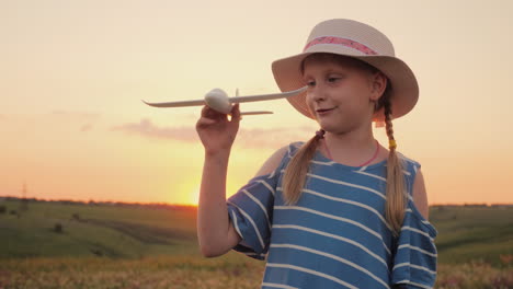 a girl with pigtails and a hat playing with a wooden airplane at sunset the dream of long-distance t