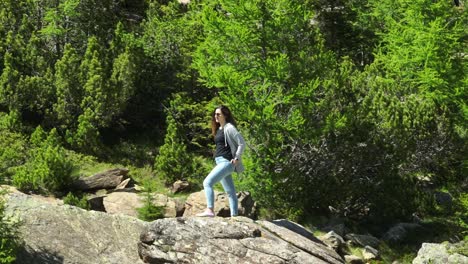 Woman-standing-on-rock-and-hikers-or-trekkers-walking-surrounded-by-nature-of-Val-Masino-in-Valtellina,-Italy