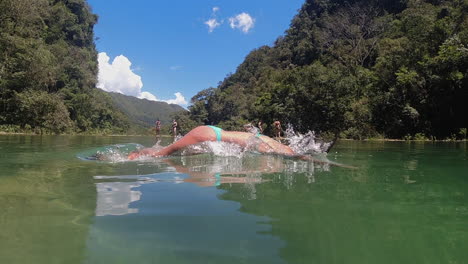 Over-Under:-Latina-Frau-Im-Bikini-Taucht-In-Den-Dschungelfluss,-Zeitlupe