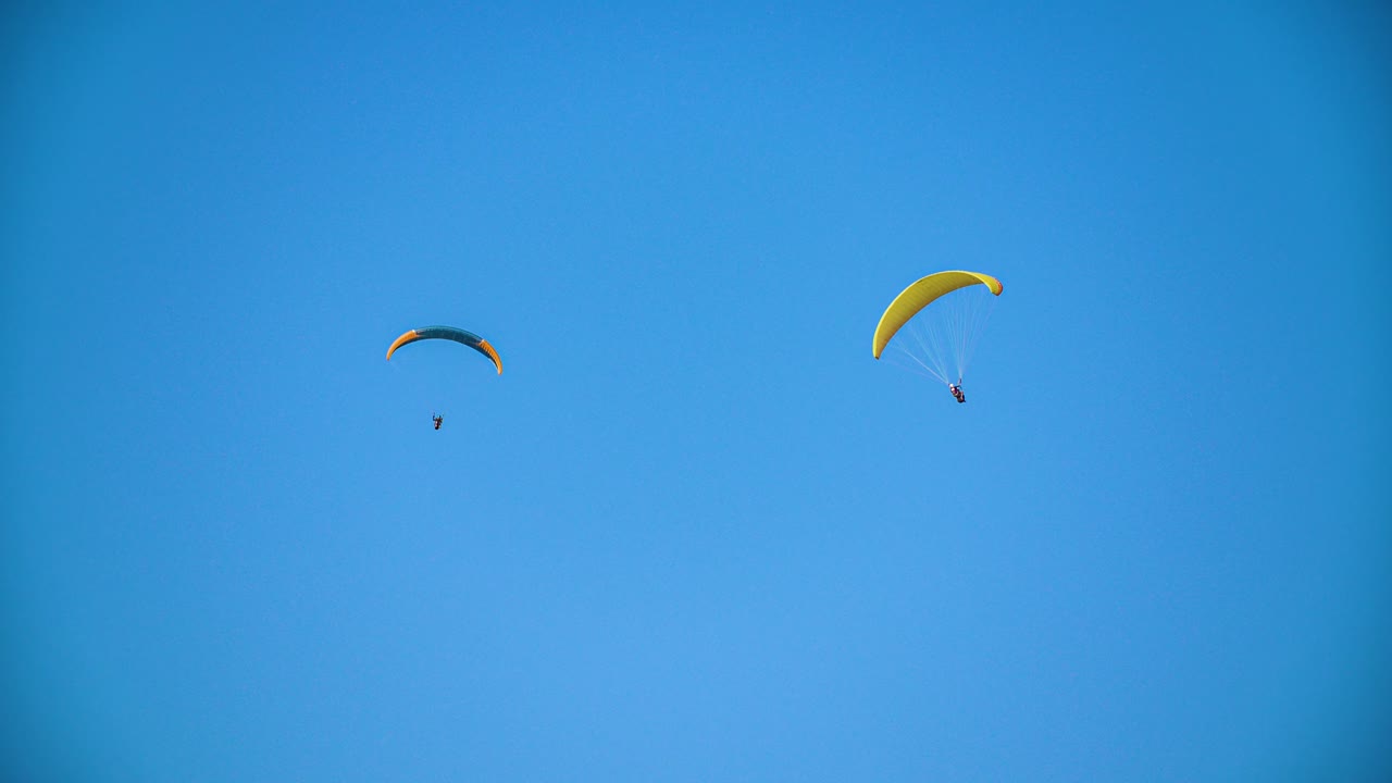 Two paragliders circle in the cloudless blue summer sky