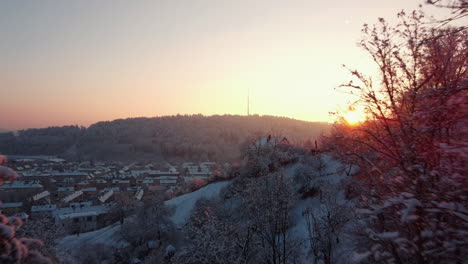 Disparo-Revelador-Volando-A-Través-De-Las-Copas-De-Los-árboles-Nevados-Que-Muestra-La-Ciudad-De-Winterthur-Contra-Un-Impresionante-Amanecer-Cálido