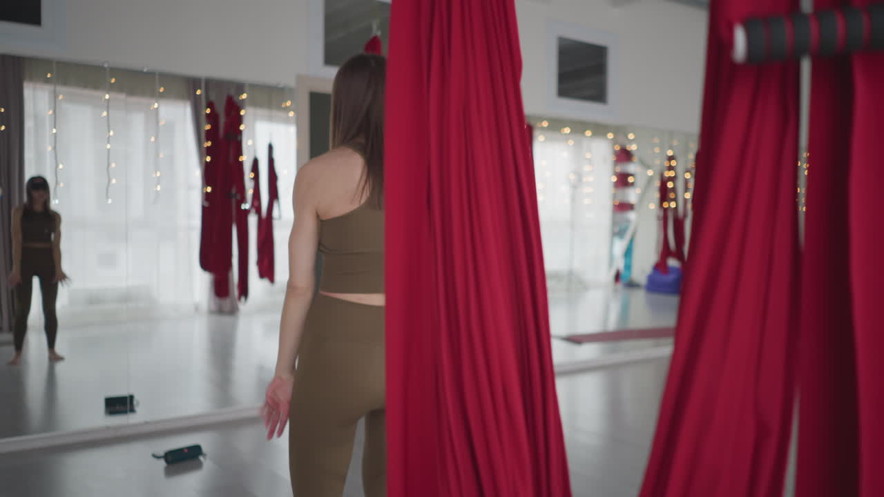 Back view of instructor and partner mirrored movements under red aerial hammocks in bright studio, gentle synchronization with occasional glances and rhythmic sway exploring balance