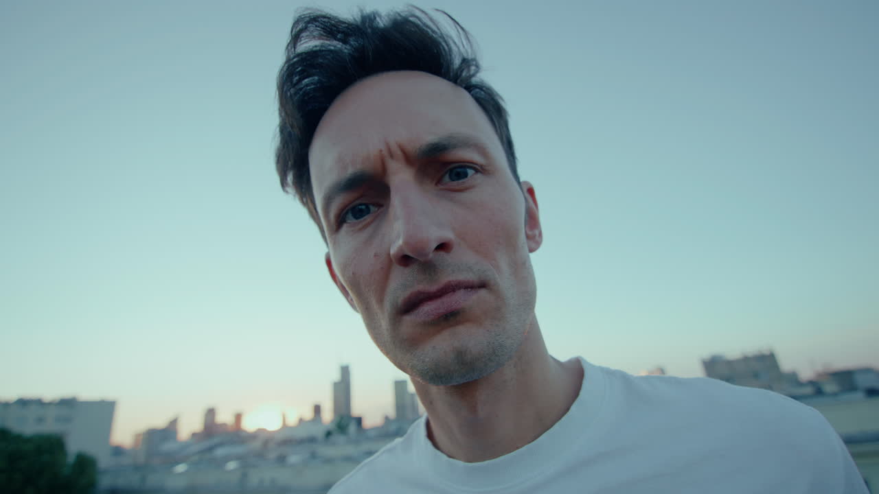Young man on city roof looks angrily into camera, handheld push-in