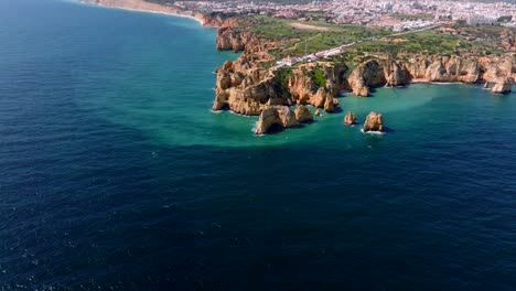 Aerial-video-from-a-partly-cloudy-day-on-the-Algarve-Coast,-as-the-drone-moving-closer-to-the-coast-it's-slowly-panning-down-highlighting-the-aqua-tones-in-the-water