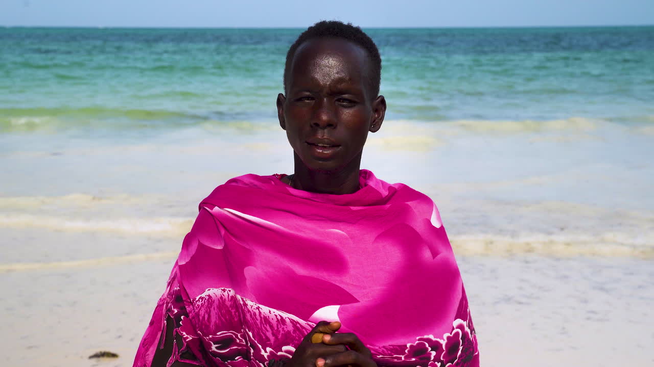Afrikansk man i rosa kläder på vit sandstrand, närbild.