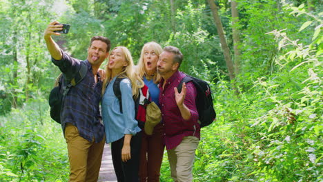 group of friends posing for selfie in countryside taking picture on phone as they hike along path