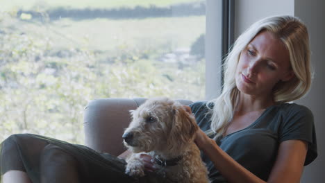 woman relaxing in chair by window at home with pet dog